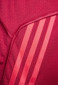Tessuto atletico rosso con un motivo testurizzato e tre strisce verticali rosa. Sono visibili dettagli delle cuciture e accenti lisci.