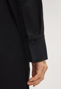Zwarte shirtboord met een gladde textuur, een getailleerde pasvorm en een knoopsluiting op de manchette, met nauwkeurige stikdetails.