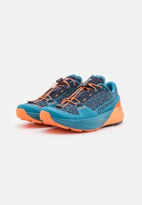 Trailrunningschoenen in teal en oranje, met een gestructureerde bovenkant, een verstelbaar vetersysteem en een duurzame zool voor grip.