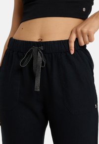 Black drawstring pants made of soft fabric with an elastic waistband, featuring front pockets and a contrast stitched ribbon tie.