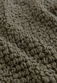 Tissu brun avec un tricot dense, bouclé et texturé créant une surface douce et en relief avec des plis et des ombres irréguliers.