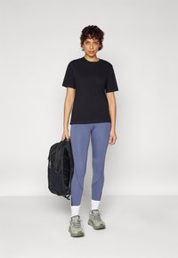 Fekete pamut póló, világoskék leggings, szürke sportcipők és egy fekete hátizsák cipzáras részletekkel. Egyszerű, funkcionális dizájn.