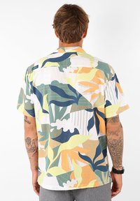 Chemise à manches courtes avec un motif de feuilles en vert, jaune et orange sur fond blanc ; col boutonné ; tissu léger.