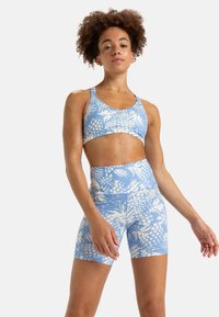 Un reggiseno sportivo di colore blu chiaro e pantaloni corti a vita alta presentano un motivo floreale bianco. Il tessuto appare liscio con un design aderente.