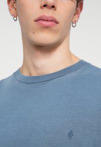 T-shirt en coton bleu clair avec un col rond et des manches courtes, présentant un petit logo brodé sur la poitrine, texture lisse.