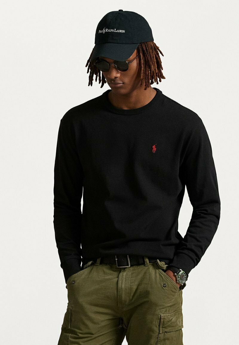 Maglietta nera a maniche lunghe con un piccolo logo rosso, abbinata a pantaloni cargo verde oliva. Un cappellino nero e occhiali da sole completano l'outfit.