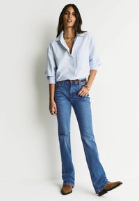 Hele sinine triibuline triiksärk, mille varrukad on rullitud, kombineeritud pooleldi laiade siniste teksade ja pruuni jalanõudega. Lihtsad ehteaktsendid.