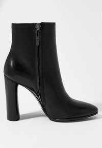 Bottine en cuir noir à bout pointu, fermeture zippée à l'arrière et talon épais. Texture lisse avec une finition brillante.