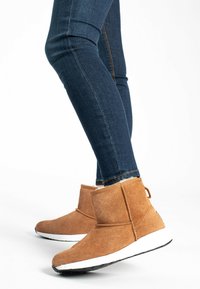 Ruskean mokkanahka ankle-botter valkoisilla pohjilla ja teksturoidulla vuorilla, yhdistettynä tummansinisiin skinny-farkkuihin. Botissa on vedettävä lenkki takana.