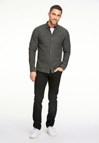 Grijze langwerpige mouw shirt met een button-down kraag en borstzak, gecombineerd met zwarte broek en witte sneakers. Zachte textuur, casual pasvorm.