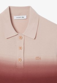 Polo dégradé rose clair à bourgogne, avec un col côtelé, une patte de boutonnage à trois boutons et un logo brodé sur la poitrine.