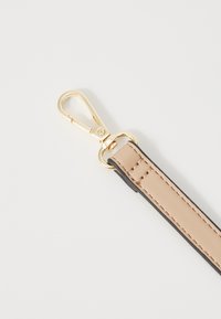 Beige keinonauha mustilla reunoilla, jossa on kultainen metallinen klipsi ja ompeluyksityiskohta pitkin pituutta. Ihanteellinen esineiden kiinnittämiseen.