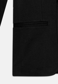 Detail čierneho blejzra s horizontálnym náprsným vreckom s lemom a dolným nášivným vreckom na prednej ľavej strane.