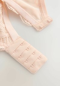 Gros plan sur une fermeture de soutien-gorge rose clair avec trois rangées d'agrafes et un détail en dentelle fine sur des bretelles en tissu.