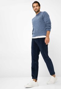 Blå tekstureret strikket sweater, cremefarvet undertrøje, mørke kordfløjlsbukser og hvide sneakers. Løs pasform med ribbede manchetter. Simpelt design.