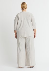 Helles graues, locker sitzendes Oberteil mit Dreiviertelärmeln und weitem Hosen. Glatte Stoffoberfläche, minimalistisches Design, klare Linien.