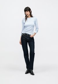 Jasnoniebieski prążkowany top z długim rękawem i małym logo, zestawiony z ciemnoniebieskimi prostymi jeansami. Dopełnieniem stylizacji są czarne botki za kostkę.