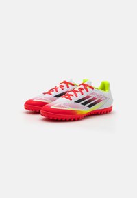 Botas de fútbol sintéticas con un upper rojo y blanco, rayas negras y acentos en amarillo neón. Suela con textura para mayor tracción.