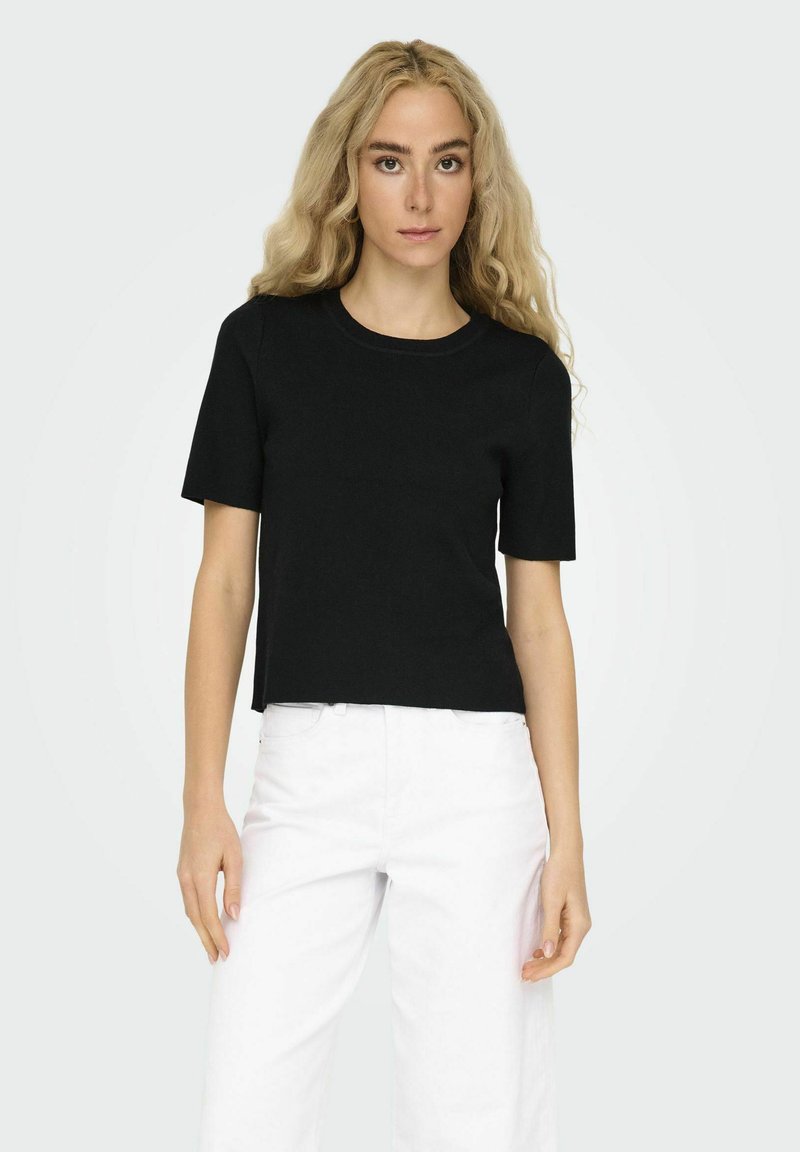 T-shirt cropped nero a maniche corte con scollo rotondo. Realizzato in un tessuto morbido e testurizzato. Abbinato a pantaloni bianchi a vita alta.