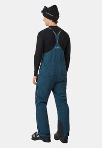 Blauwe skioveralls met verstelbare banden en ritszakken, gemaakt van een duurzaam materiaal. Heeft een versterkte onderkant en een ergonomisch ontwerp.