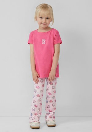 T-shirt en coton rose avec un motif de coquillage, associé à un pantalon rose à motifs comportant des dessins de coquillages. La tenue comprend des chaussures de couleur claire.