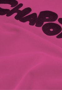 Tessuto fucsia con lettere nere in grassetto e texture che recitano "CHAPO". Il materiale ha una superficie liscia con una leggera elasticità.