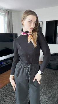 Svart långärmad topp med figursydd design, kombinerad med lösa svarta byxor med dragsko. En färgglad mönstrad scarf är knuten runt halsen.