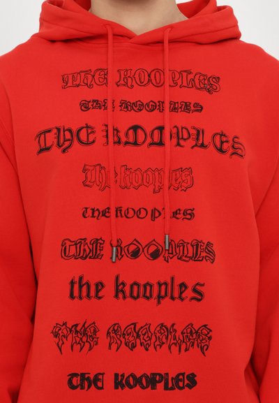 Rode hoodie met herhaalde zwarte tekst in verschillende lettertypes: "THE KOOPLES," "the kooples," en "THE ROOPLES." Met een trekkoord in de capuchon en een zachte textuur.