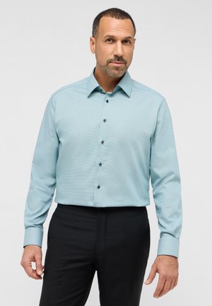 Himmelblaues Langarmshirt mit strukturiertem Muster, mit Kragen und dunklen Knöpfen, getragen mit schwarzen Hosen.