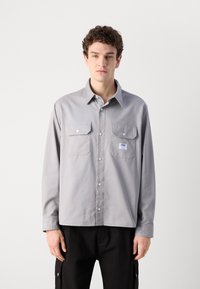 Gray long-sleeve shirt made of cotton, featuring two front pockets, a button-down collar, and a small label on the left pocket.