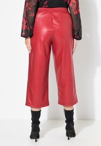 Culotte in eco-pelle rossa con gamba larga e vita elastica, caratterizzate da una texture liscia e una lunghezza cropped, abbinate a stivaletti neri alla caviglia.