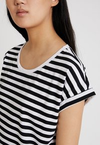Černobíle pruhované tričko s kulatým výstřihem a ohrnutými rukávy, vyrobené z měkkého materiálu, s rovnoměrnými horizontálními pruhy.