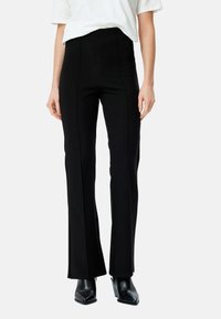 Pantalons noirs évasés à taille haute, fabriqués en tissu extensible, avec des détails de couture à l'avant et une texture lisse. Assortis à des bottes à talons noires.