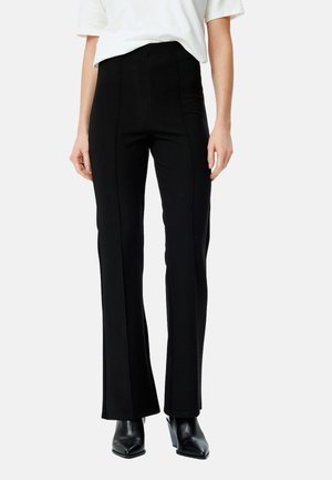 Pantalons noirs évasés à taille haute, fabriqués en tissu extensible, avec des détails de couture à l'avant et une texture lisse. Assortis à des bottes à talons noires.