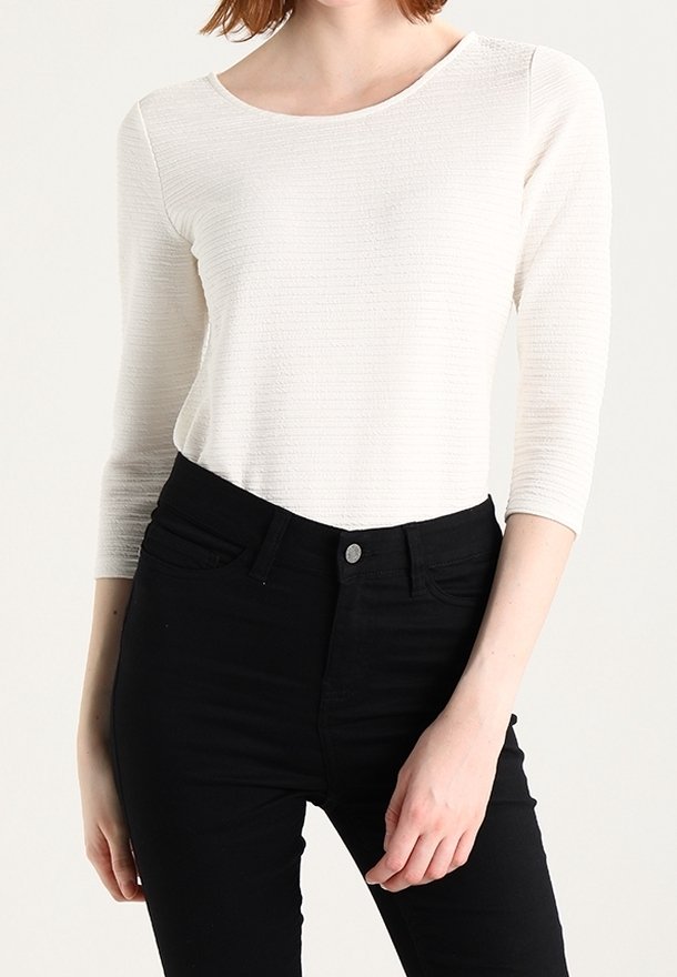 White, textured long-sleeve top with a crew neckline, paired with high-waisted black jeans featuring a front button and pockets.