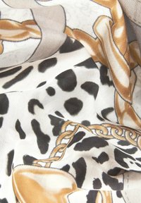 Sciarpa di seta con stampa animale in bianco e nero e motivo a catena dorata. Texture morbida, caduta elegante e colori vivaci in tutto.