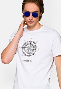 Biała bawełniana koszulka z grafiką kompasu w kolorze czarnym i szarym, z napisem "PODRÓŻUJ Z STYLEM" pod spodem. Okrągły dekolt, krótkie rękawy.