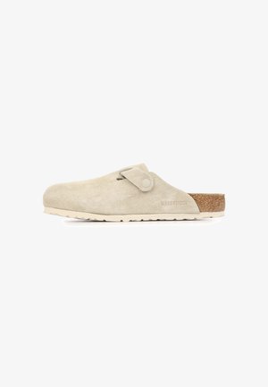 Zueco beige de ante con pala ajustable, plantilla de corcho y suela de goma texturizada, marca Birkenstock en el lateral.