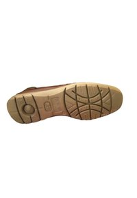 La semelle extérieure de la chaussure marron présente un design texturé avec des rainures pour l'adhérence, un talon renforcé et un bouton circulaire près de la zone de l'arche.