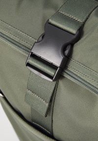 Olive green fabric buckle bag featuring a sturdy plastic clasp, textured surface, and zipper detailing for secure closure and access.