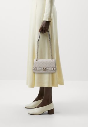 Sac à main gris clair avec un motif gaufré, une anse en chaîne et un détail en nœud. Associé à une robe jaune pâle et des escarpins blancs à bout fermé.