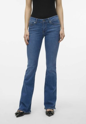 Blauwe flare jeans van denim, met een middelhoge taille, voorzakken en een lichte vervaging. Gecombineerd met zwarte puntige schoenen.