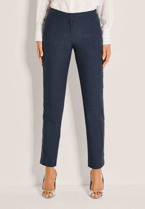 Donkerblauwe, op maat gemaakte broek van een gladde stof, met een slanke pasvorm, enkellengte en een strak tailleband. Zilverkleurige schoenen met hoge hakken.