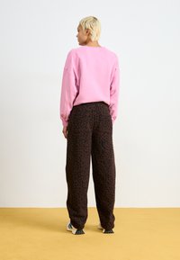 Rosa übergroßes Sweatshirt kombiniert mit braunen Leopardenmusterhosen. Das Outfit zeichnet sich durch eine lockere Passform und weiche Texturen aus.