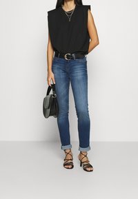 Musta hihaton toppi, jossa on pehmustetut olkapäät, siniset slim fit -farkut, musta krokotiilikuosiset käsilaukku ja mustat remmillä varustetut korkokengät.