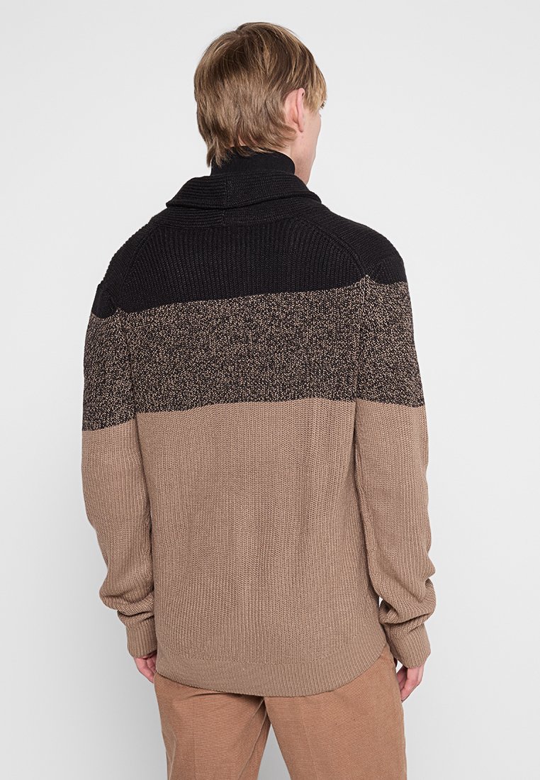 Langärmliger Pullover mit hohem Kragen, der ein Farbblockdesign in Schwarz, gesprenkelt Grau und Beige aufweist. Strukturiertes Strickmaterial und gerippte Bündchen.