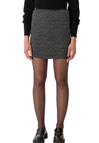Mini-jupe noire et grise à motifs, coupe droite, tissu texturé, associée à des collants noirs et des mocassins brillants. Un simple pull noir en haut.
