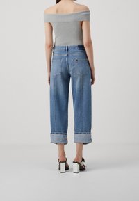 Top gris claro sin mangas combinado con jeans de denim azul de corte holgado, doblados en los tobillos; presenta dos bolsillos traseros y un detalle de cremallera.
