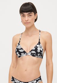 Svart bikini topp med trekantet design og hvite blomster mønstre. Justerbare tynne stropper og senter knutepunkt detalj.