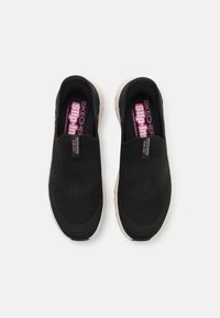 Scarpe nere senza lacci con tomaia in maglia testurizzata e collo imbottito. Presentano una soletta rosa con il marchio "SKECHERS slip-in". Suola di colore crema.